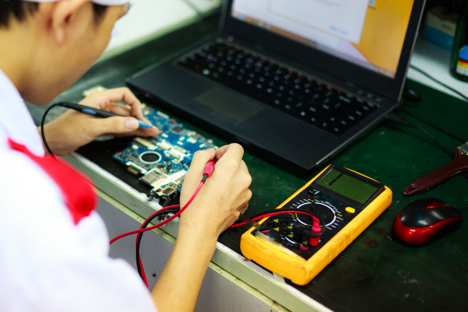 Technician testing and repairing electronic equipment with a multimeter at a workbench